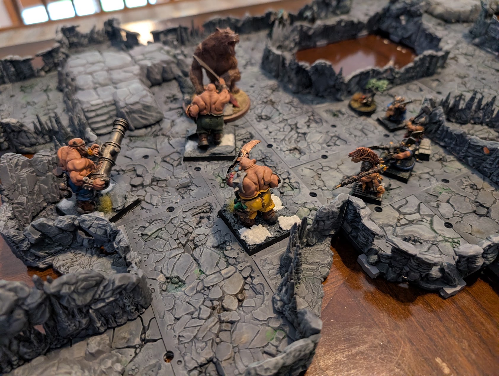 Ogre and dwarf miniatures gather in narrow stone passages surrounded by rocky cave walls.